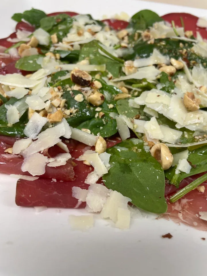 Shaved Parmigiano over bresaola, spinach, and hazelnuts on a Davanti archive plate