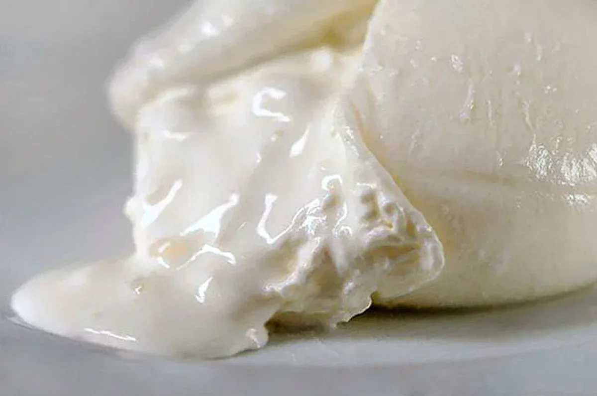 Close-up of a cut soft white cheese with creamy strands spilling onto a plate