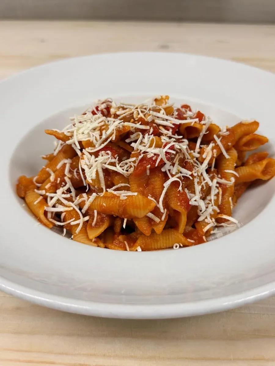 Garganelli pasta coated in red sauce and topped with grated white cheese on a white plate