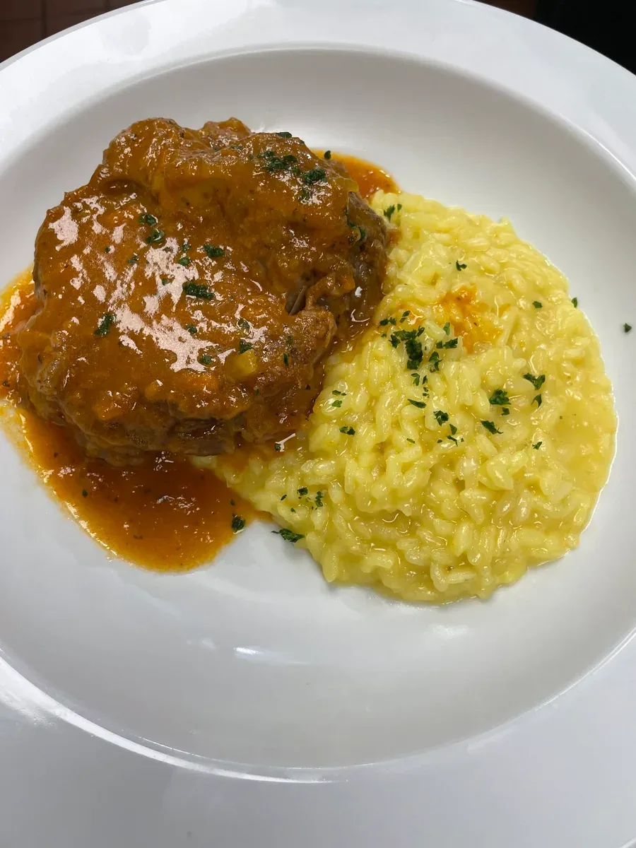 Braised veal shank beside saffron risotto on a white plate