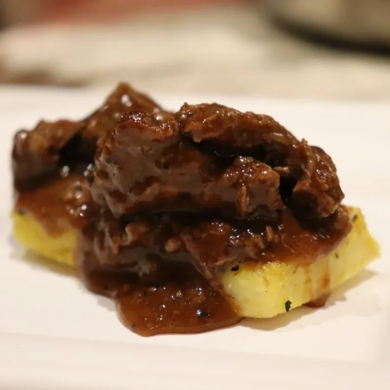 Venison stew in a dark sauce over thick yellow polenta slices on a white plate