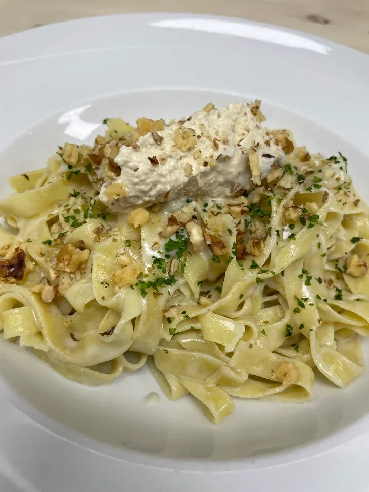 Fettuccine topped with a pale walnut sauce, chopped walnuts, and green herbs on a white plate