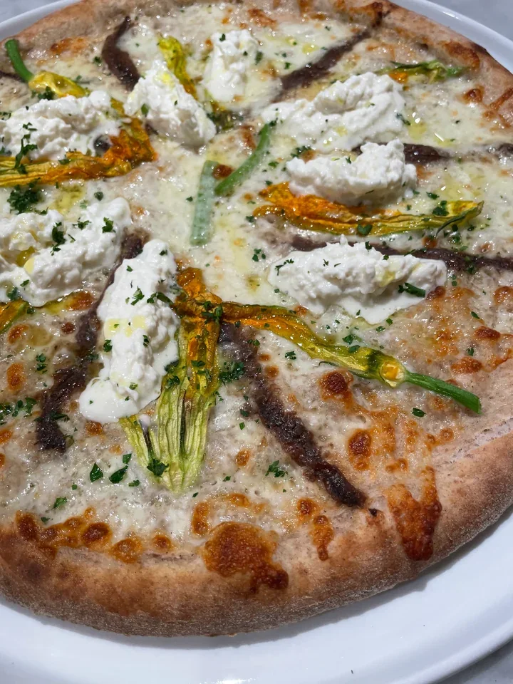 Baked pizza topped with golden squash blossoms, soft white cheese, and dark fillets
