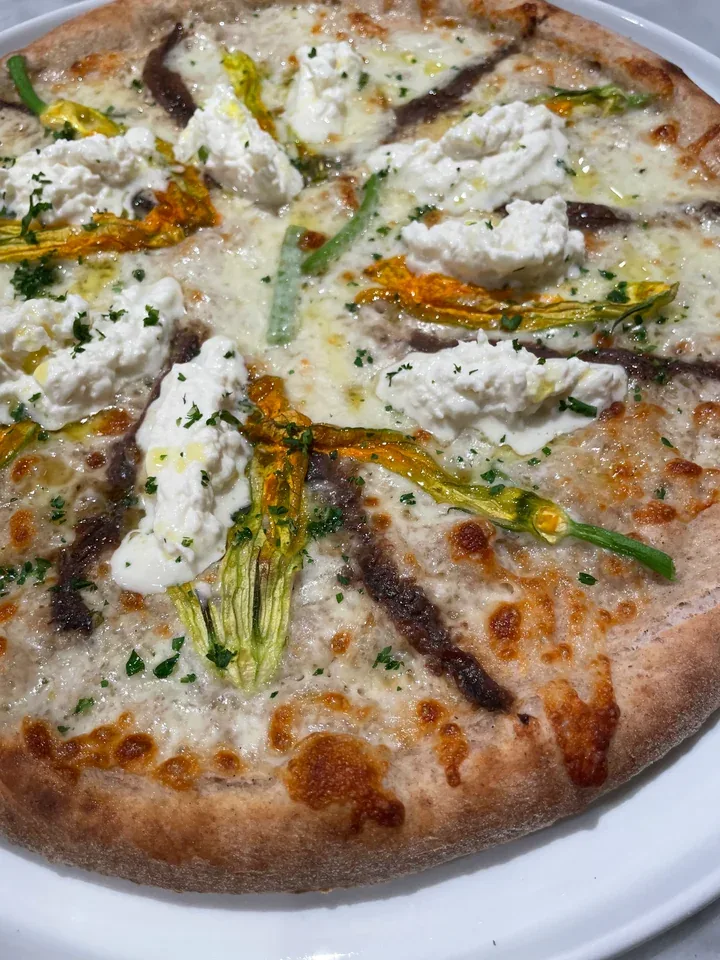 Baked pizza topped with golden squash blossoms, soft white cheese, and dark fillets