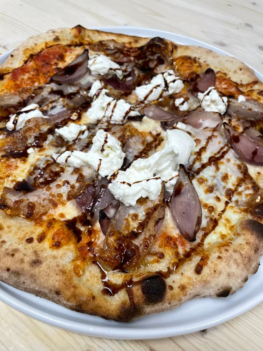 Pizza topped with porchetta, caramelized onions and dollops of stracciatella on a white plate