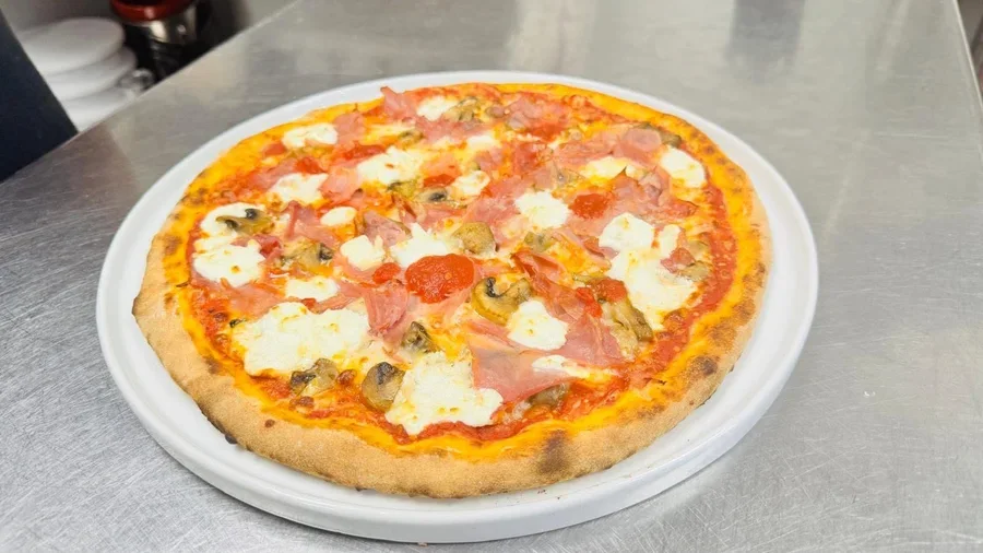 Round pizza topped with cooked ham, goat cheese and sliced mushrooms on a white plate