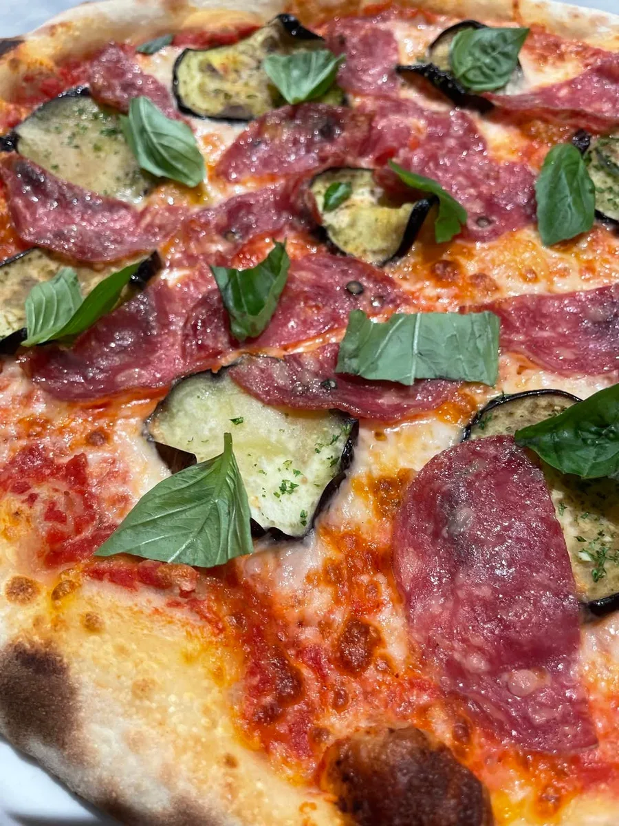 Pizza topped with eggplant rounds, salame Napoletano, mozzarella and green basil leaves