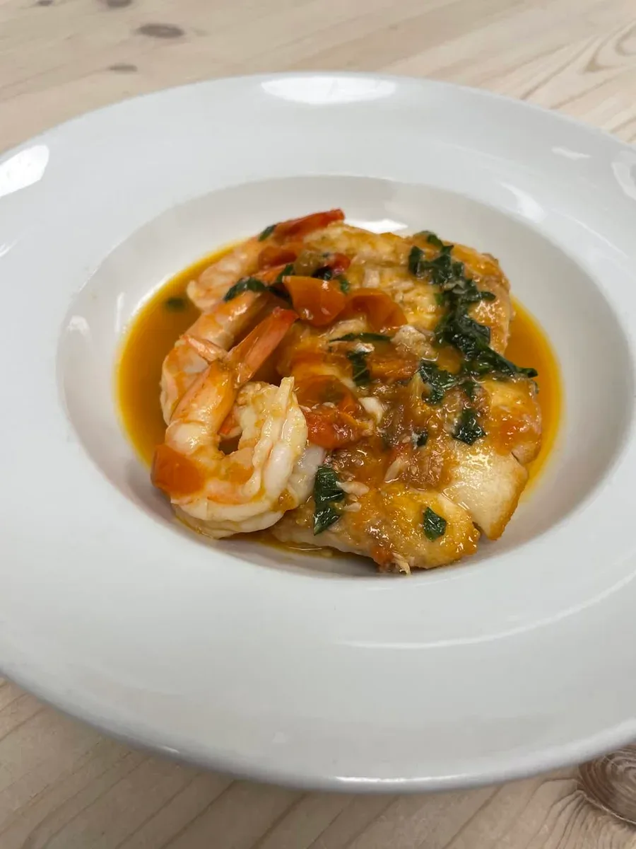 Red snapper with shrimp, tomatoes and herbs in a golden sauce on a white plate