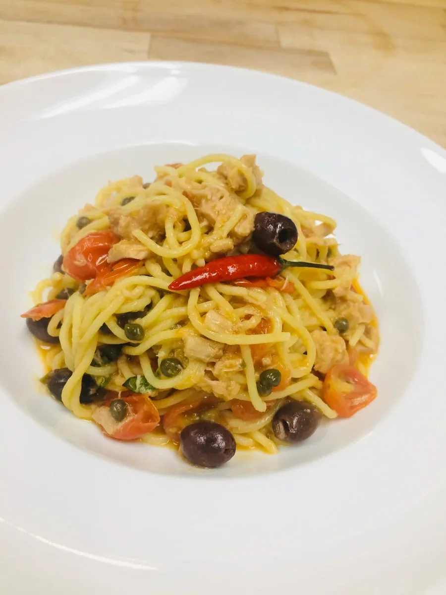 Spaghetti with tuna, grape tomatoes, black olives and capers in a white bowl