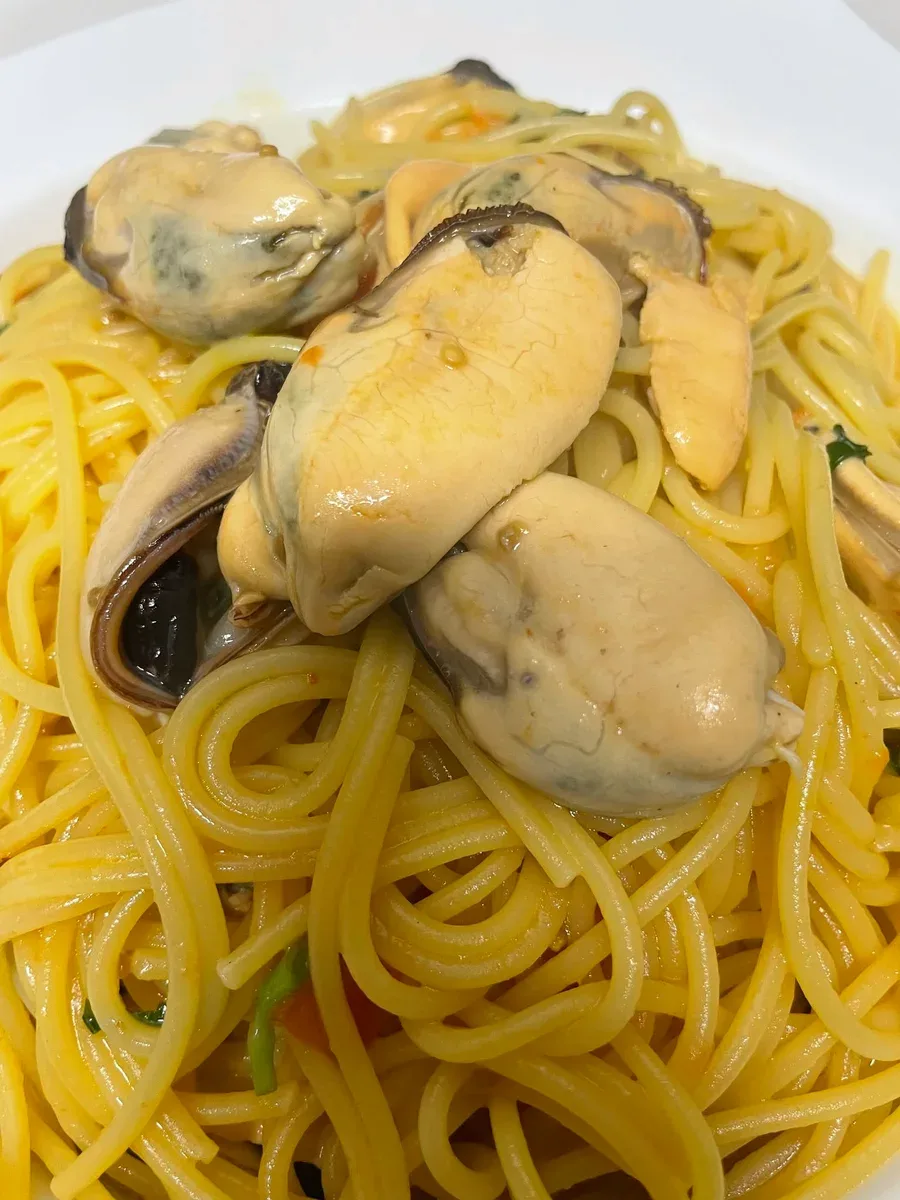 Spaghetti topped with mussels in a white bowl