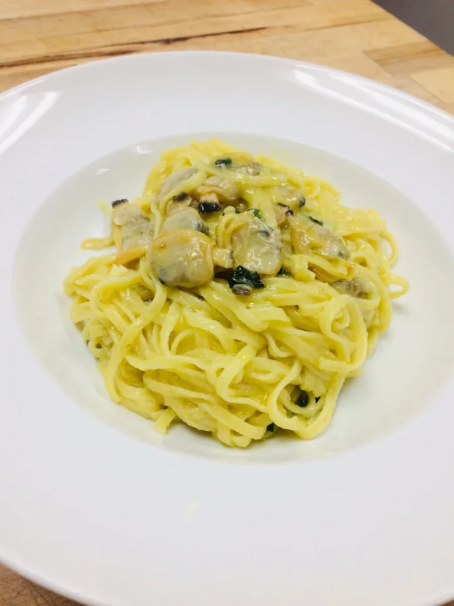 Fine tagliolini and shelled clams in a pale leek sauce on a white plate